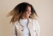 Mulher sorrindo com cabelo cacheado e natural, em movimento, mostrando uma atitude positiva e cheia de confiança.
