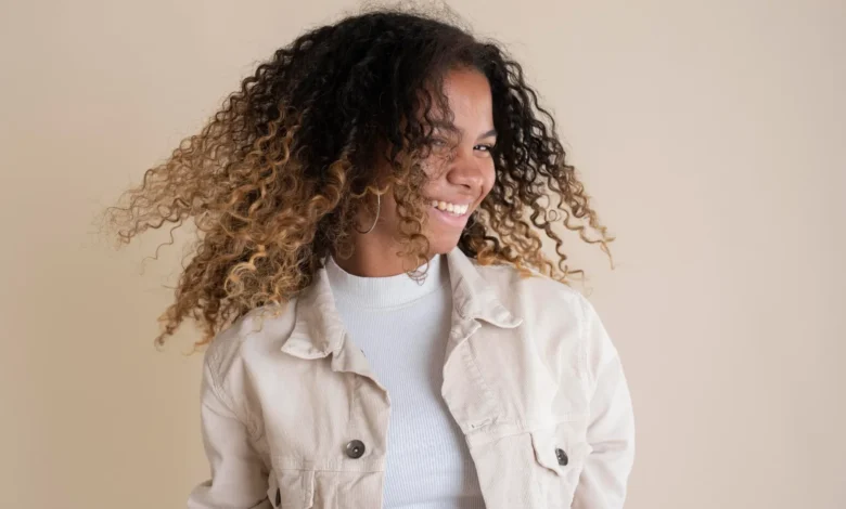 Mulher sorrindo com cabelo cacheado e natural, em movimento, mostrando uma atitude positiva e cheia de confiança.