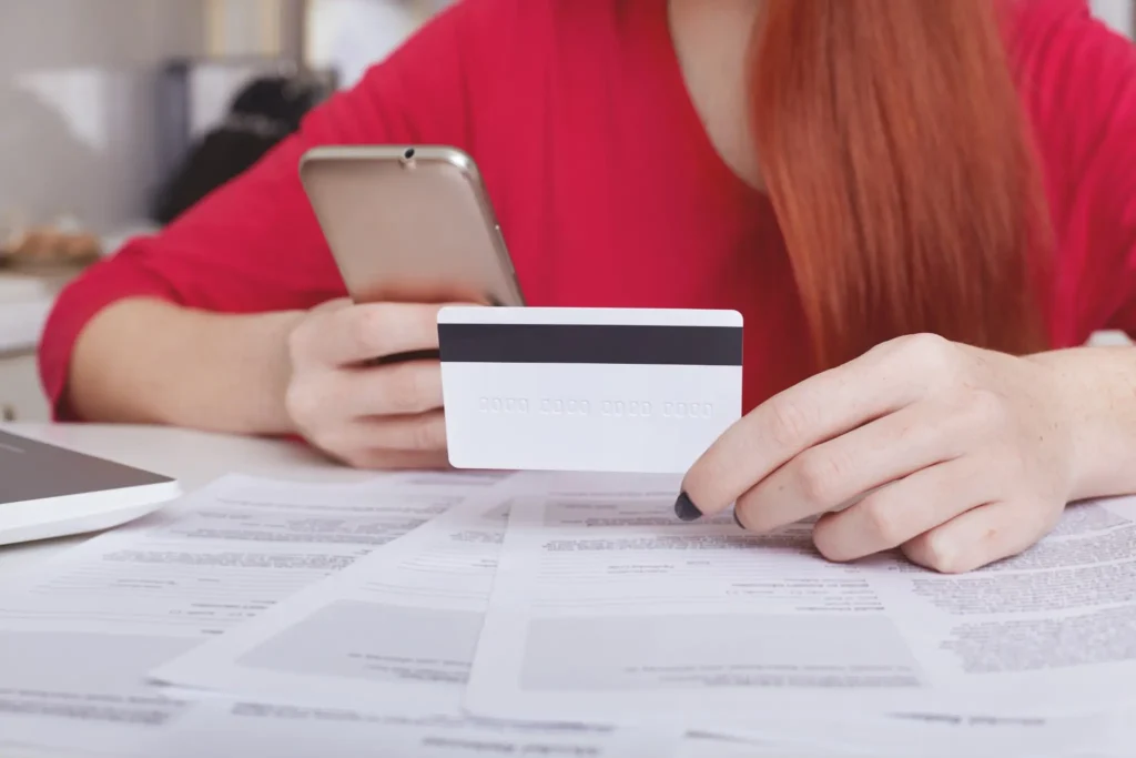 Pessoa com cartão de crédito e smartphone, organizando documentos e pagamentos