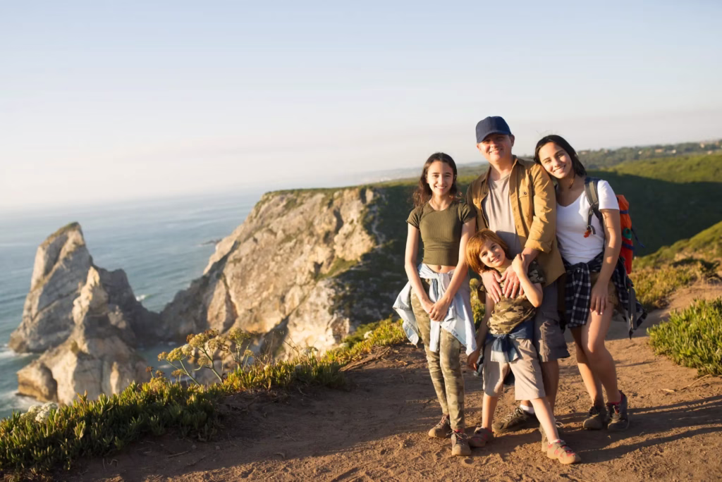 Família aproveitando um passeio ao ar livre em um cenário montanhoso, com pais e filhos sorrindo e se divertindo durante uma caminhada.