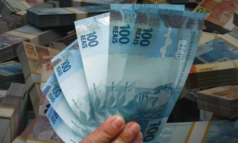 Pessoa segura notas de 100 reais, representando saque do Caixa Tem.