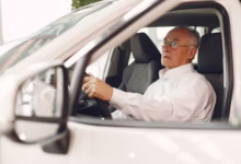 Idoso em concessionária de carros, pensativo enquanto olha para o volante, relacionado ao IPVA grátis para idosos.