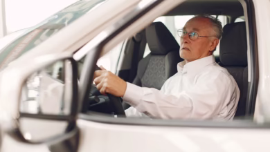 Idoso em concessionária de carros, pensativo enquanto olha para o volante, relacionado ao IPVA grátis para idosos.