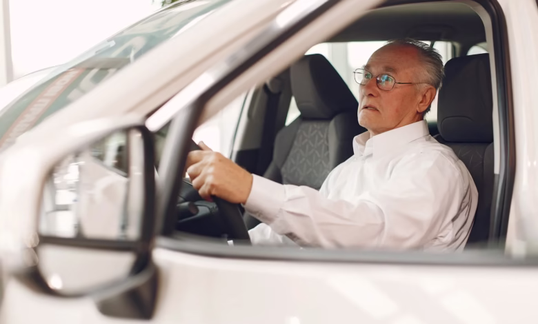 Idoso em concessionária de carros, pensativo enquanto olha para o volante, relacionado ao IPVA grátis para idosos.