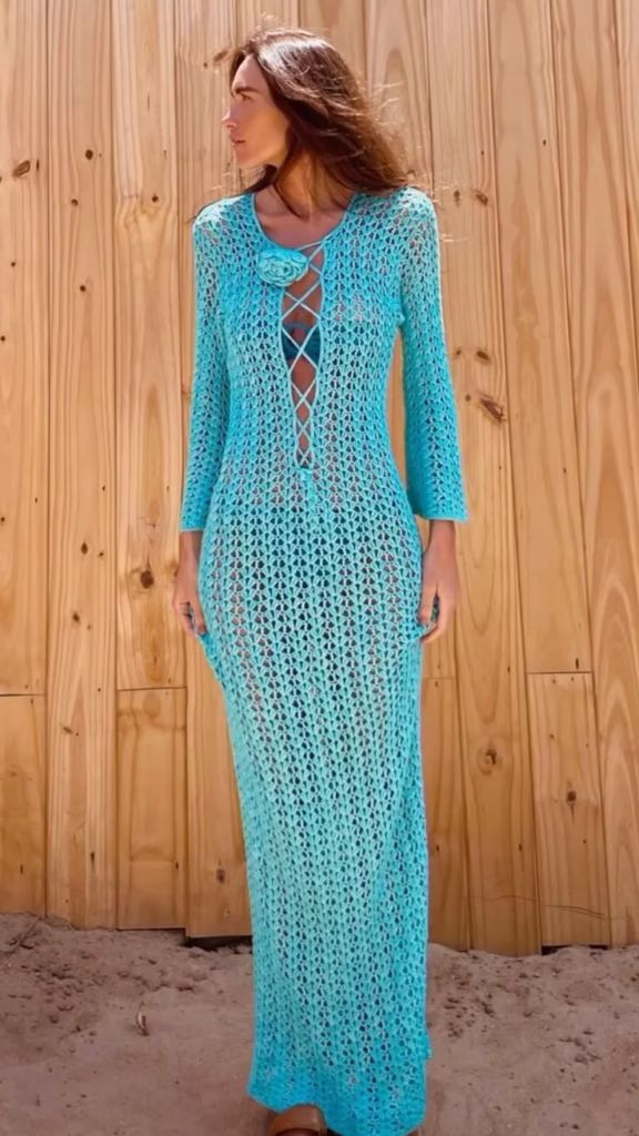 Mulher usando vestido midi de crochê azul com mangas longas, com detalhes de abertura no centro.