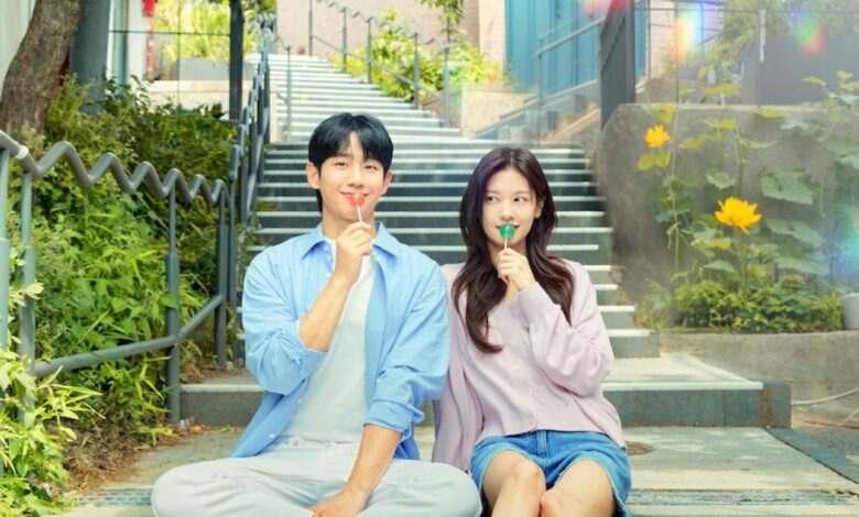 Um casal sorrindo e segurando pirulitos em frente a uma escadaria, representando um dorama romântico.