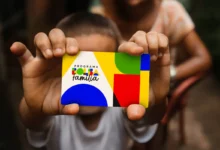 Mãos de uma criança segurando o cartão do Bolsa Família, com o logotipo do programa em destaque, simbolizando a notícia sobre o possível reajuste do benefício em 2026