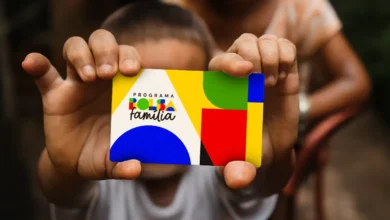 Mãos de uma criança segurando o cartão do Bolsa Família, com o logotipo do programa em destaque, simbolizando a notícia sobre o possível reajuste do benefício em 2026