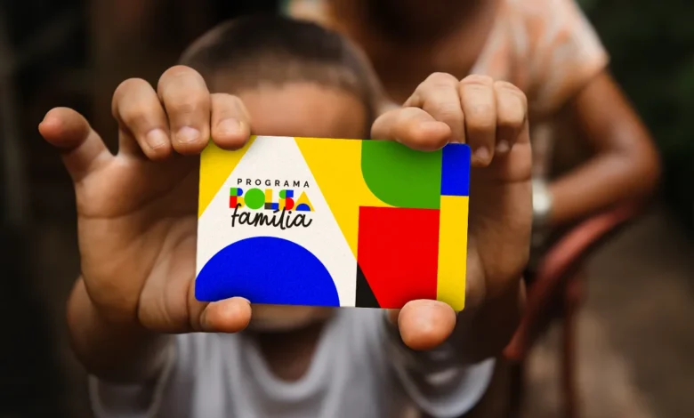 Mãos de uma criança segurando o cartão do Bolsa Família, com o logotipo do programa em destaque, simbolizando a notícia sobre o possível reajuste do benefício em 2026