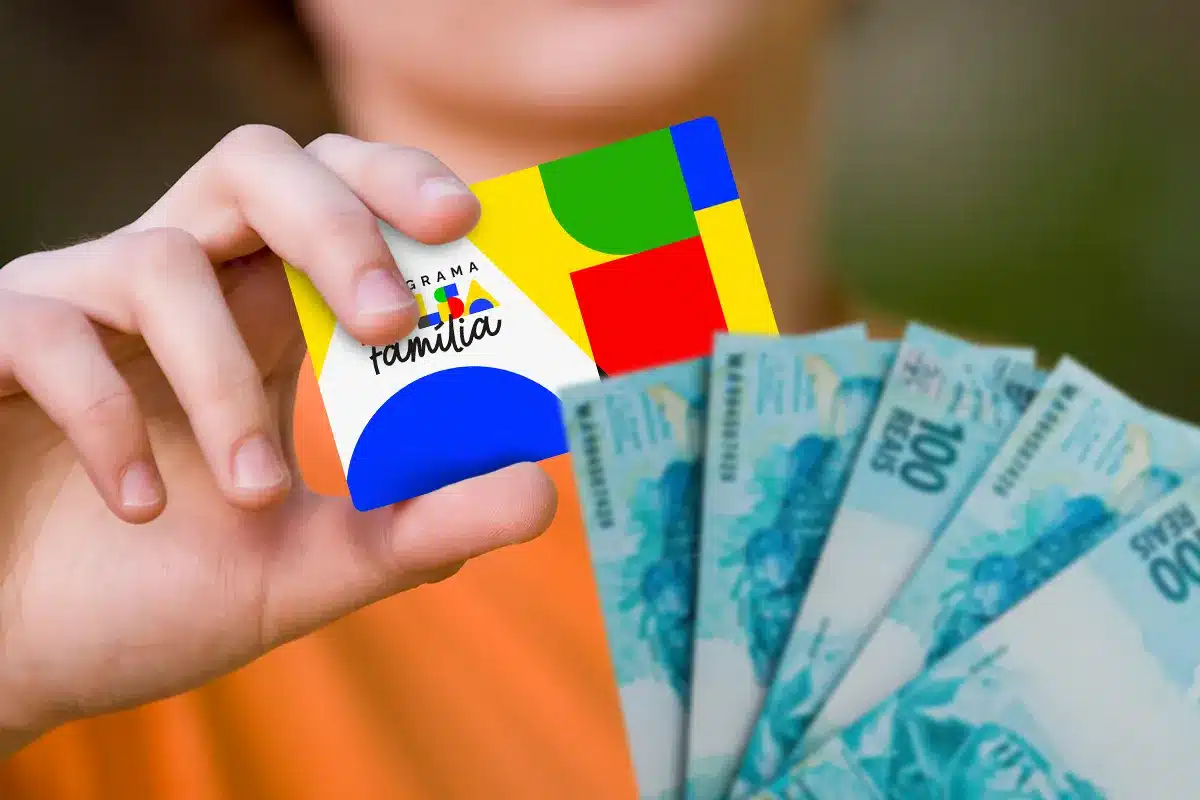Mão segurando o cartão do Bolsa Família e cédulas de R$100, simbolizando a distribuição do benefício de outubro.