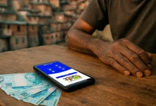 Pessoa visualizando o aplicativo Bolsa Família em um celular, com notas de 100 reais ao lado.