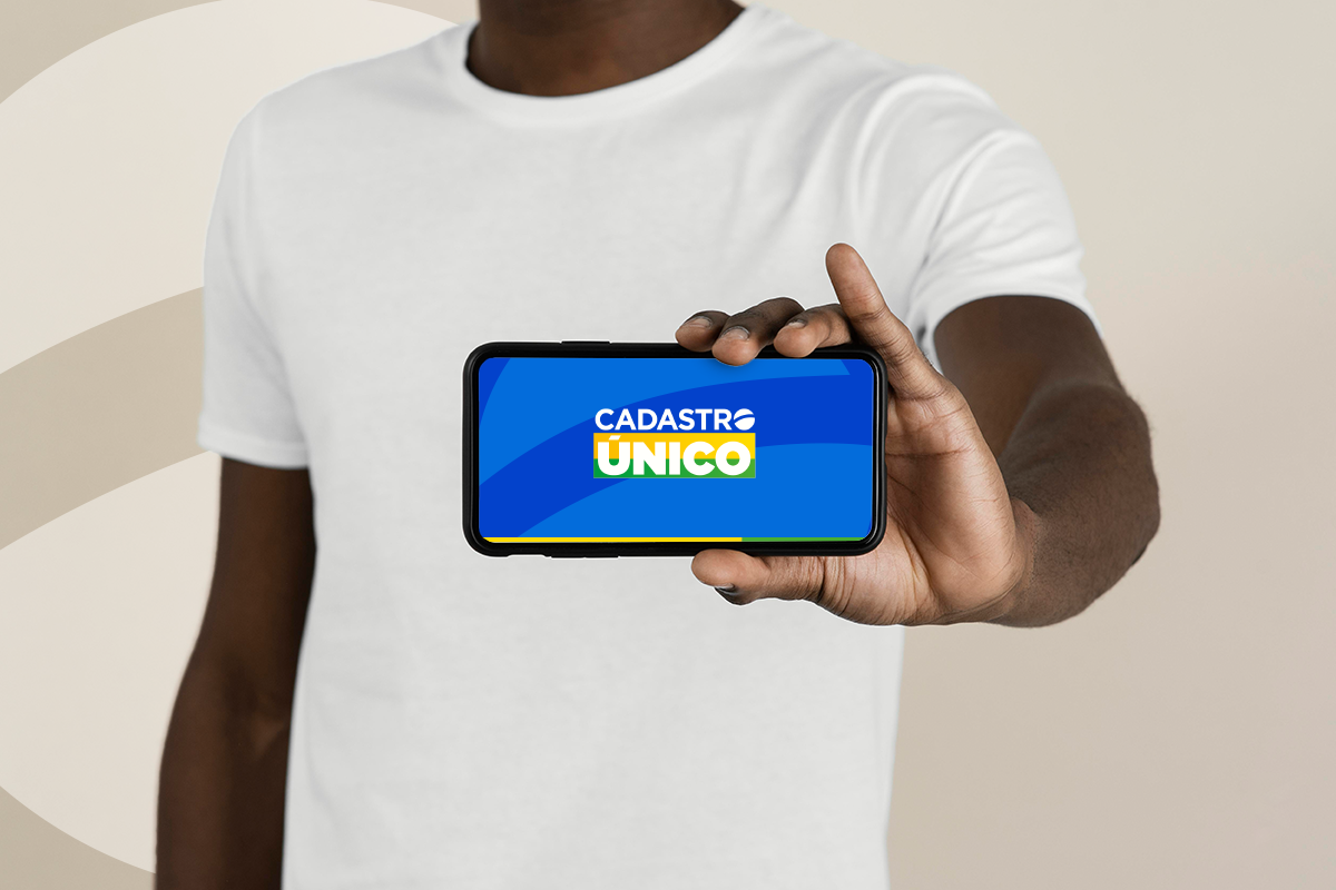 Mãos de uma pessoa segurando um smartphone com o logo do Cadastro Único exibido na tela. A imagem representa o acesso digital e a notificação sobre a atualização de dados.