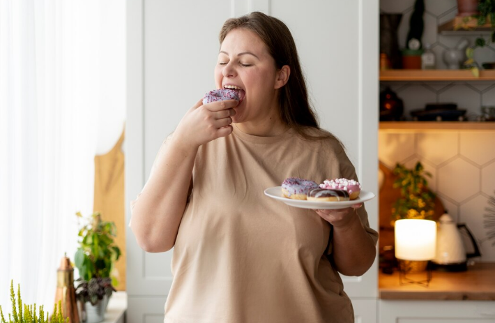 Mulher com sobrepeso comendo um donut, simbolizando hábitos alimentares que podem levar à gordura no fígado.