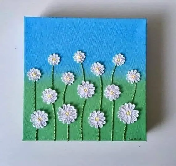 Quadro de crochê com flores brancas sobre fundo azul e verde, ideal para decoração personalizada e composta.