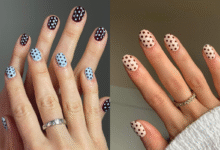 Mãos com unhas decoradas com estampa de bolinhas (poá) em diferentes cores, uma em azul claro com bolinhas pretas e a outra em tom de nude com bolinhas marrons.