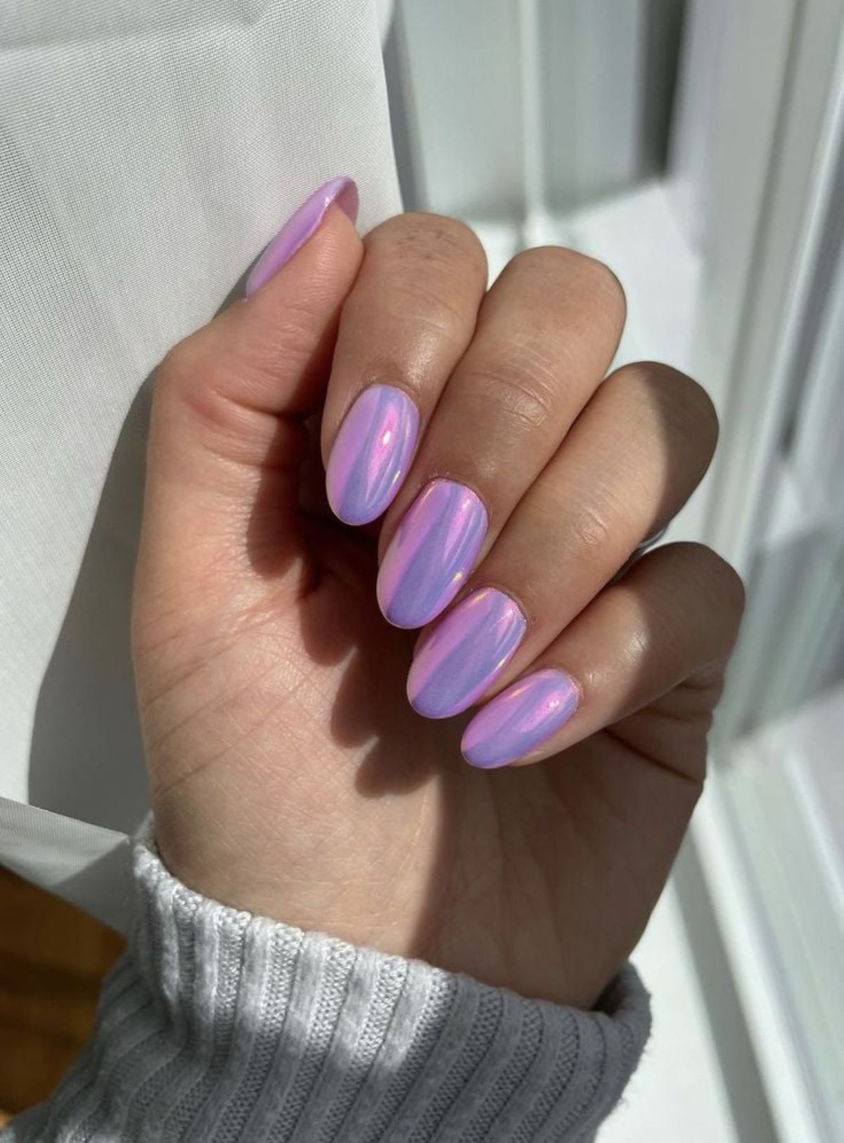 Unhas com esmalte lilás metálico e reflexos iridescentes, realçando o efeito futurista da cor