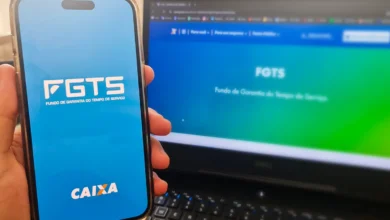 Uma mão segura um maço de notas de R$ 100 ao lado de um smartphone que exibe o logo do FGTS. A imagem simboliza a regularização financeira de débitos relacionados ao Fundo de Garantia.