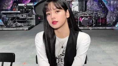 Lisa do BLACKPINK em ambiente de palco, com cabelo longo e liso, vestindo uma camiseta branca com estampa