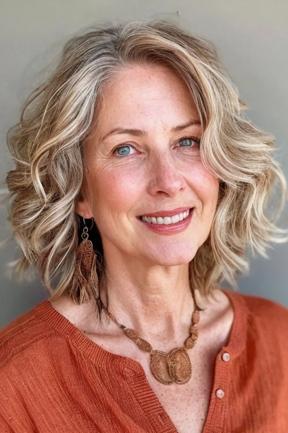 Mulher com cabelo loiro platinado suave, usando uma blusa laranja e acessórios naturais.