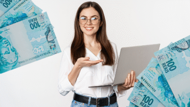 Mulher sorrindo segura notebook com notas de 100 reais ao redor, simbolizando ganho financeiro ou dinheiro virtual.