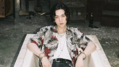 Suga do BTS, em estilo casual, relaxando em um cenário artístico