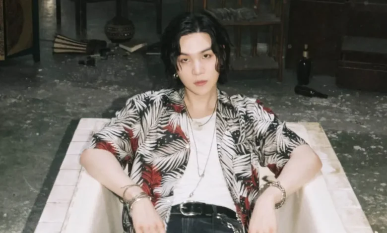 Suga do BTS, em estilo casual, relaxando em um cenário artístico