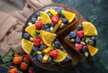 Bolo com frutas frescas da estação, coberto com chocolate e decorado com laranjas, morangos, mirtilos e amêndoas.