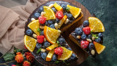 Bolo com frutas frescas da estação, coberto com chocolate e decorado com laranjas, morangos, mirtilos e amêndoas.