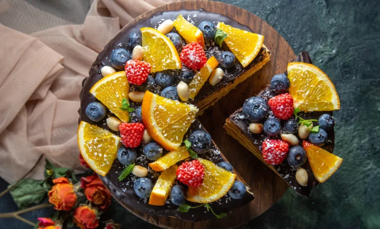 Bolo com frutas frescas da estação, coberto com chocolate e decorado com laranjas, morangos, mirtilos e amêndoas.