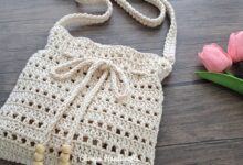 Bolsa tiracolo de crochê bege, feita à mão, sobre uma mesa de madeira.