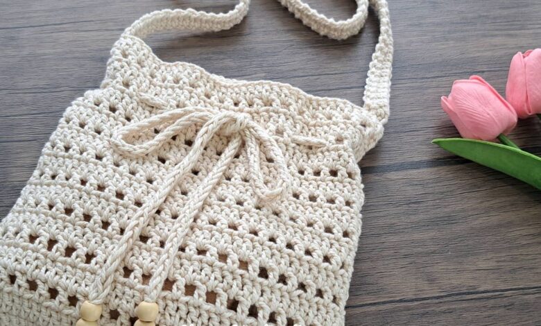 Bolsa tiracolo de crochê bege, feita à mão, sobre uma mesa de madeira.