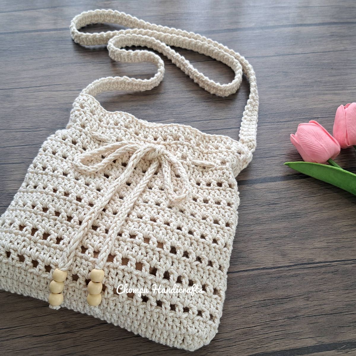 Bolsa tiracolo de crochê bege, feita à mão, sobre uma mesa de madeira.