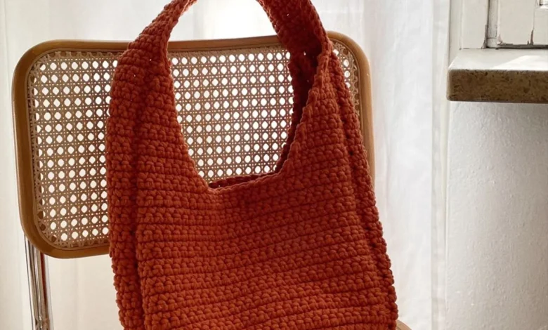 Bolsa de crochê laranja feita à mão sobre uma cadeira de vime, em ambiente iluminado