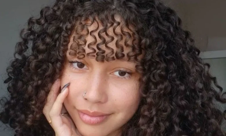 Mulher com cabelo cacheado e franja, estilo moderno e volumoso, mostrando como modelar cabelos cacheados com franja