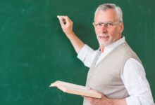 Professor sênior escrevendo em quadro-negro com giz, representando as mudanças nas regras de aposentadoria para educadores.