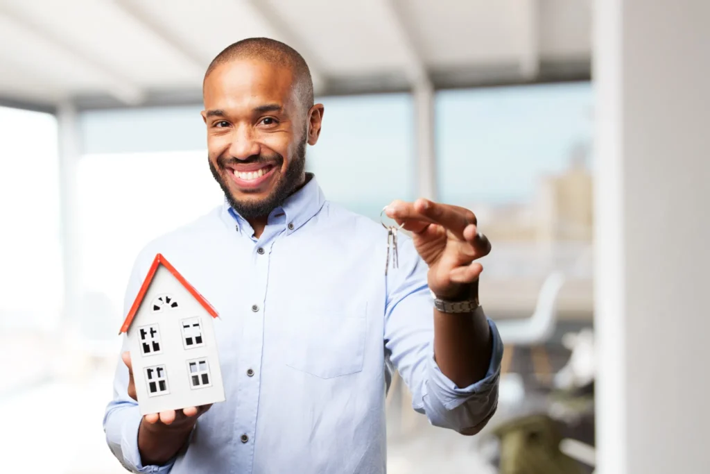 Homem feliz segurando miniatura de casa e chaves, simbolizando a conquista do sonho da casa própria.