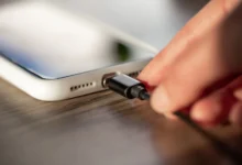 Imagem de uma mão conectando um cabo de carregador a um celular, simbolizando o ato de carregar o dispositivo.