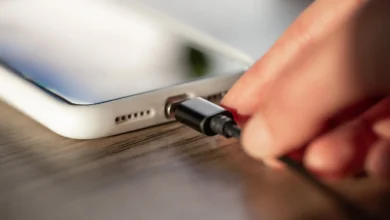 Imagem de uma mão conectando um cabo de carregador a um celular, simbolizando o ato de carregar o dispositivo.