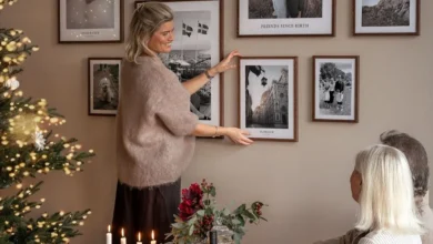 Pessoa ajustando quadros decorativos na parede com uma árvore de Natal ao fundo em uma sala de estar aconchegante.