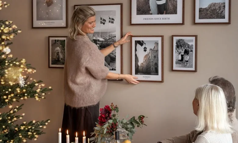 Pessoa ajustando quadros decorativos na parede com uma árvore de Natal ao fundo em uma sala de estar aconchegante.