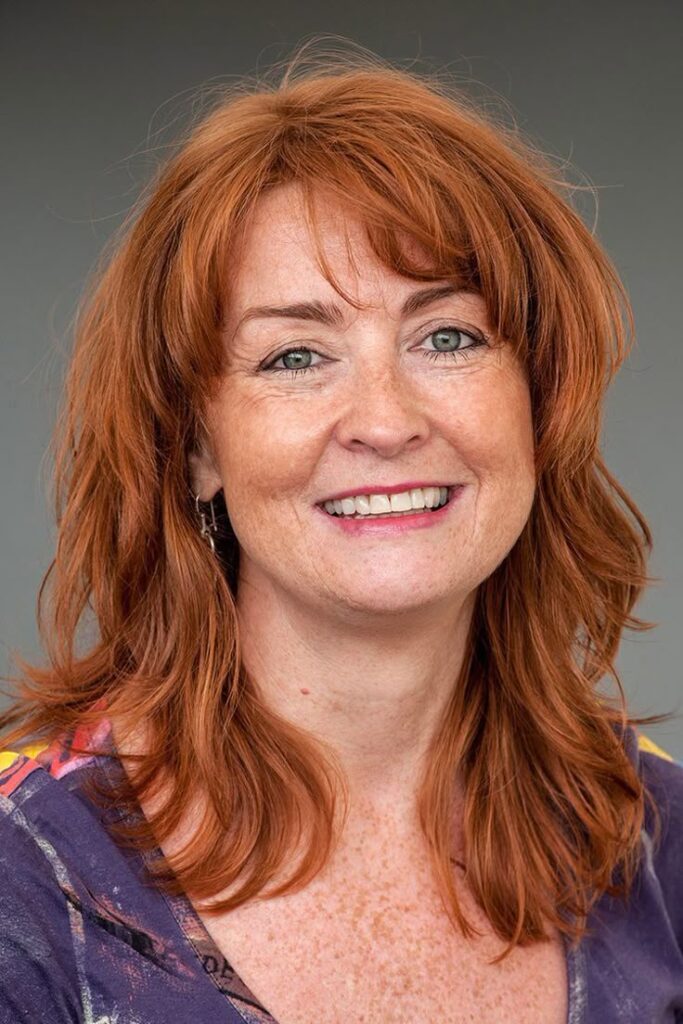Retrato de uma mulher madura com cabelo ruivo acobreado, sorrindo. A cor destaca os tons vibrantes do ruivo para mulheres 50+.