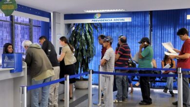 Uma fila de pessoas, incluindo idosos, aguarda atendimento em um balcão da Previdência Social no Brasil.
