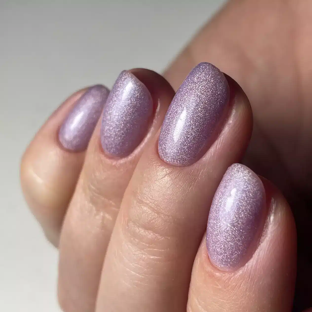 Unhas com esmalte lilás holográfico, mostrando o brilho cintilante da cor da moda no verão europeu