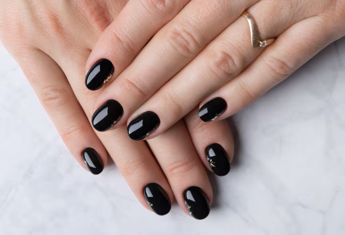 Mãos com unhas pintadas de esmalte preto brilhante e aplicação sutil de glitter.