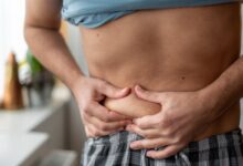 Pessoa apertando a barriga, indicando preocupação com a gordura corporal e a saúde do fígado.