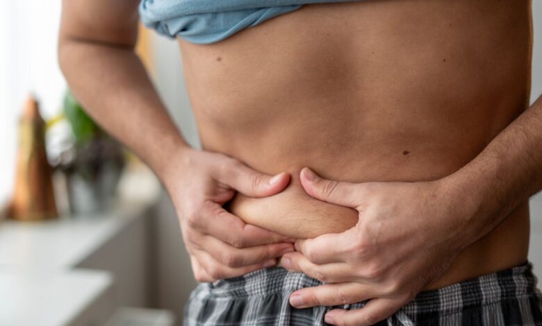Pessoa apertando a barriga, indicando preocupação com a gordura corporal e a saúde do fígado.