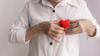 Mulher de meia-idade segurando um coração de crochê vermelho próximo ao peito, simbolizando cuidado e saúde cardíaca. Ideal para artigos sobre prevenção de infarto.