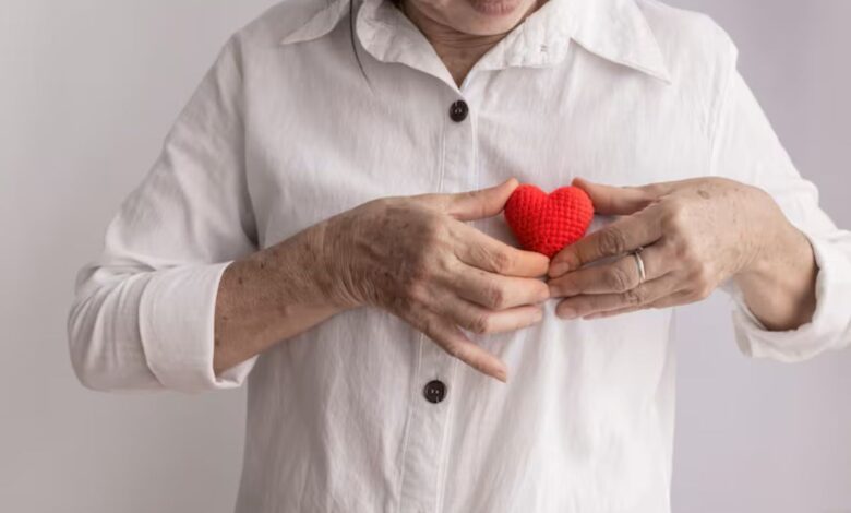 Mulher de meia-idade segurando um coração de crochê vermelho próximo ao peito, simbolizando cuidado e saúde cardíaca. Ideal para artigos sobre prevenção de infarto.