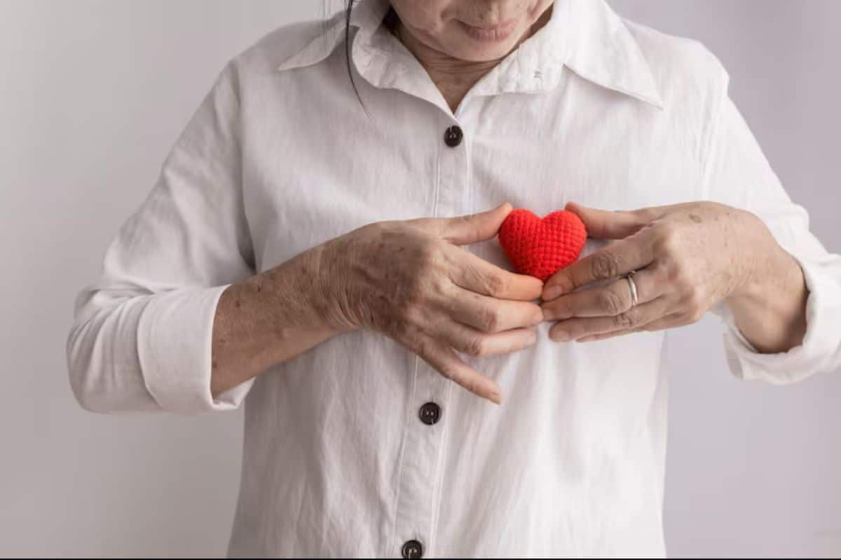 Mulher de meia-idade segurando um coração de crochê vermelho próximo ao peito, simbolizando cuidado e saúde cardíaca. Ideal para artigos sobre prevenção de infarto.