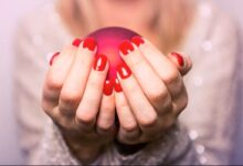 Mãos de uma mulher segurando uma esfera vermelha com unhas pintadas de esmalte vermelho vivo.